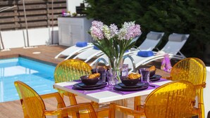 Un espace repas aménagé au bord de la piscine, avec une table dressée pour quatre personnes, entourée de chaises orange, et une piscine en arrière-plan.