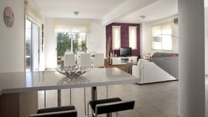 Une cuisine moderne avec un îlot central, un coin repas avec des chaises, un canapé et un téléviseur dans le salon.