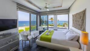 A modern hotel room with a large bed, a TV, a balcony with a view of the sea, and a ceiling fan. - You and Your Family Will Love This Beachfront Villa, Protaras Villa 1526 (Paralimni)