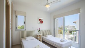 Une chambre d’hôtel avec deux lits simples, un ventilateur de plafond, une fenêtre donnant sur des immeubles et un radiateur.