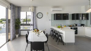 A modern kitchen with a central island, a dining area with a table and chairs, and a view through large windows. - The Secret to Enjoying Your 5 Star Villa With Large Private Pool, Protaras Villa 1493 (Paralimni)