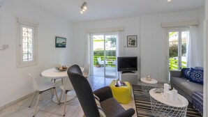 Una sala de estar moderna con un sofá, una mesa de comedor con sillas, un televisor y un balcón con vistas.