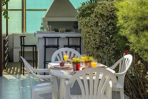 An outdoor dining area with a table set for two, surrounded by white chairs. There is a small bar area with a counter and chairs in the background. - You and Your Family Will Love This Villa Close to the Beautiful Town of Protaras, Protaras Villa 1441 (Paralimni)