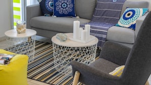 Una sala moderna con un sofá gris, cojines estampados, un sillón amarillo y una alfombra a rayas.