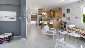 A modern kitchen with a central island, white bar stools, and a dining area with a colorful sofa. - Ultimate Beachside Luxury: Protaras Villa 1461 (Paralimni)