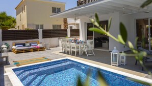 A modern outdoor pool area with a covered patio, a dining set, and a lounge area. - Ultimate Beachside Luxury: Protaras Villa 1461 (Paralimni)