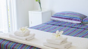 A neatly made bed with striped bedding, a white nightstand with a vase of flowers, and two towels with flowers on a white bedspread. - Ultimate Beachside Luxury: Protaras Villa 1461 (Paralimni)