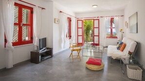 A living room with a TV, a glass coffee table, a sofa, and a wicker ottoman. - Discover Perfect Holiday Escape in Protaras, 1411 (Paralimni)