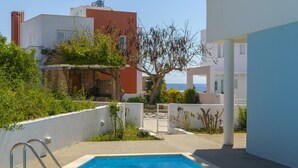 A swimming pool with a metal ladder, surrounded by white walls and greenery, with buildings and a view of the sea in the background. - The Ultimate Guide to Renting Your Luxury 3 Bedroom Villa Minutes From the Beach, Protaras Villa 1530 (Paralimni)