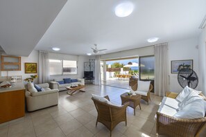A spacious living area with a sofa, chairs, a dining table, and a view of the outdoors. - 5 Star Beachfront Villa, Protaras Villa 1536 (Paralimni)