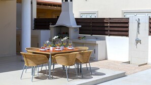 An outdoor patio with a round table set for dining, surrounded by wicker chairs. - 5 Star Beachfront Villa, Protaras Villa 1536 (Paralimni)