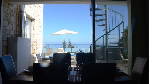 Ein Essbereich mit Tisch und Stühlen, einem Sonnenschirm und Blick auf das Meer durch eine offene Tür.