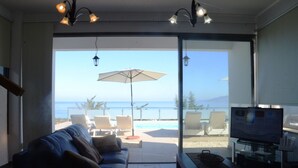 Ein Wohnzimmer mit einer Couch, einem Fernseher und Blick auf einen Pool und den Ozean.