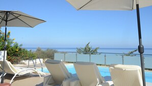 Ein Poolbereich mit Liegestühlen und Sonnenschirmen mit Blick auf das klare, blaue Meer.