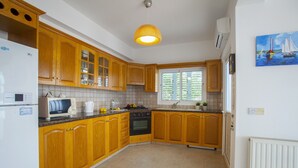 A kitchen with wooden cabinets, a stove, a sink, and a window with blinds. - Imagine Your Family Renting This Luxury Villa With Large Private Pool, Protaras Villa 1543 (Paralimni)