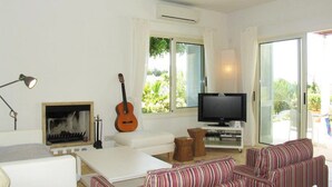 A living room with a white sofa, a striped couch, a guitar, a TV, and a fireplace. - How to Rent Your Own Villa in Paphos With Fantastic Private Pool, Paphos Villa 1418 (Neo Chorio)