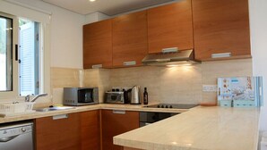 A modern kitchen with wooden cabinets, a microwave, a kettle, and a stove. - How to Rent Your Own Villa in Paphos With Fantastic Private Pool, Paphos Villa 1418 (Neo Chorio)