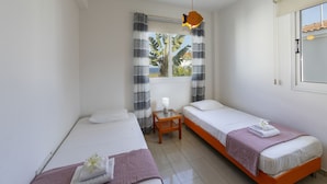 A hotel room with two single beds, a small table, a window with curtains, and an air conditioning unit. - Imagine You and Your Family Renting This Luxury Villa Minutes From the Beach, Protaras Villa 1501 (Paralimni)