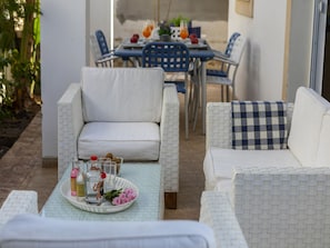 Un espace patio aménagé avec des meubles en osier, une table sur laquelle se trouve un plateau rempli d’objets, et une table à manger en arrière-plan.
