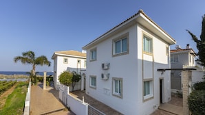 A two-story white building with a tiled roof, a gated entrance, and a view of the sea. - Imagine You and Your Family Renting This Luxury Villa Minutes From the Beach, Protaras Villa 1501 (Paralimni)