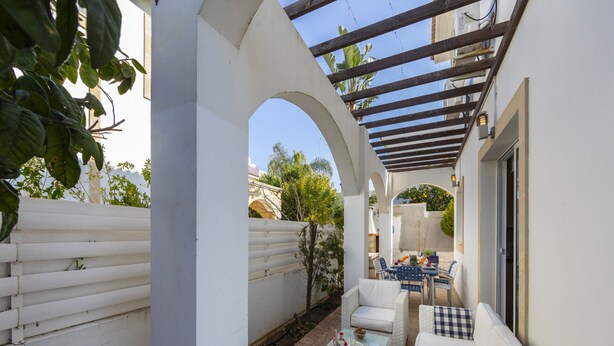 A covered patio area with white wicker furniture, a table with a glass top, and a pergola structure. - Imagine You and Your Family Renting This Luxury Villa Minutes From the Beach, Protaras Villa 1501 (Paralimni)
