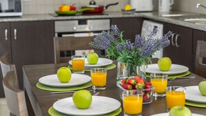 Une table mise pour le petit-déjeuner, avec des assiettes de fruits, des verres de jus d’orange et un vase rempli de fleurs.