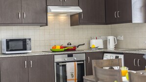 Une cuisine compacte avec des meubles de couleur bois foncé, un four à micro-ondes, une bouilloire, un grille-pain et un égouttoir à vaisselle.