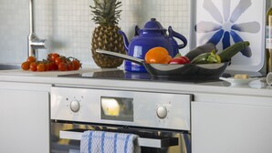 Une cuisine équipée d’un four en acier inoxydable, d’une bouilloire bleue et d’un saladier rempli de légumes posé sur le plan de travail.
