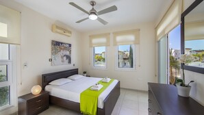 Un dormitorio con cama, mesitas de noche, ventilador de techo, ventana con vistas y aire acondicionado instalado en la pared.