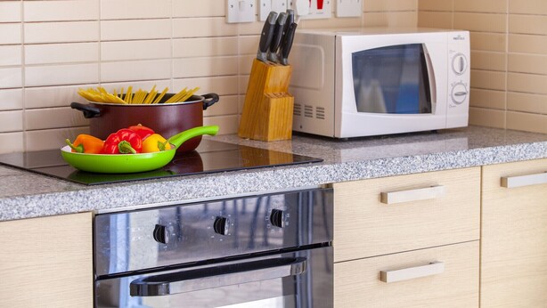 A kitchen with a microwave, stove, and a bowl of vegetables on the counter. - Unforgettable 5-star Escape: Protaras Villa 1476 (Paralimni)