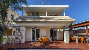 Ein modernes, zweistöckiges Haus mit Swimmingpool, Sitzgelegenheiten im Freien und einer Pergola.