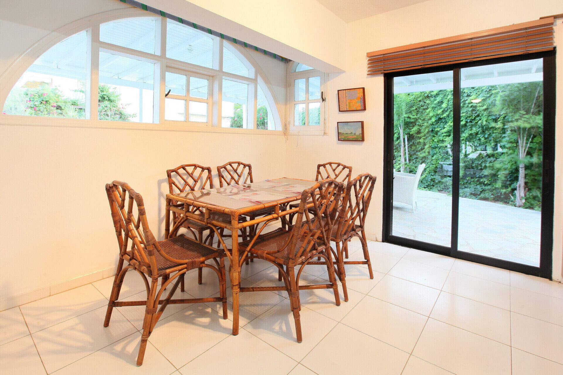 A dining area with a round table and six wicker chairs, large windows with a view of greenery, and a sliding glass door.