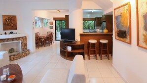 A living room with a TV, wooden furniture, a fireplace, and a kitchen area with a bar. - The Ultimate Guide to Renting Your Luxury 3 Bedroom Villa Minutes From the Beach, Protaras Villa 1496 (Paralimni)