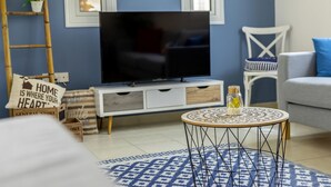 Ein Wohnzimmer mit Fernseher, einem weißen Sofa, einem gemusterten Teppich und einem kleinen Tisch mit einer Dekoration.