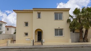 Ein zweigeschossiges Gebäude mit flachem Dach, einem zentralen Eingang mit Rundbogen und einem kleinen Balkon im zweiten Obergeschoss.