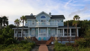 A two-story house with a front porch, a covered walkway, and a view of the surrounding greenery. - Oceanfront / Sleeps 16 / Beach Days / Screen Porch (Isle of Palms)