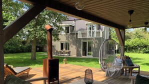 Un patio exterior con una mesa de madera, sillas y un sillón colgante. Se ve una estufa de leña al fondo.