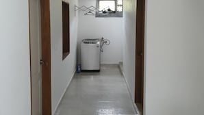 A narrow hallway with white walls and a shiny tiled floor. There are wooden doors on either side, and a washing machine is visible in the distance. - Villa del Socorro (Jardín)