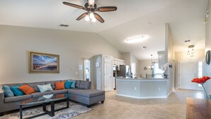 A spacious living room with a gray sectional sofa, a glass coffee table, and a ceiling fan. - Centralized, stylish getaway. Short drive to beach, shopping, downtown, Mayo! (Jacksonville)