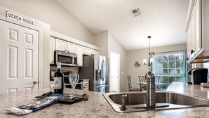 A kitchen with white cabinets, stainless steel appliances, a granite countertop, and a sign reading "BEACH HOUSE". - Centralized, stylish getaway. Short drive to beach, shopping, downtown, Mayo! (Jacksonville)