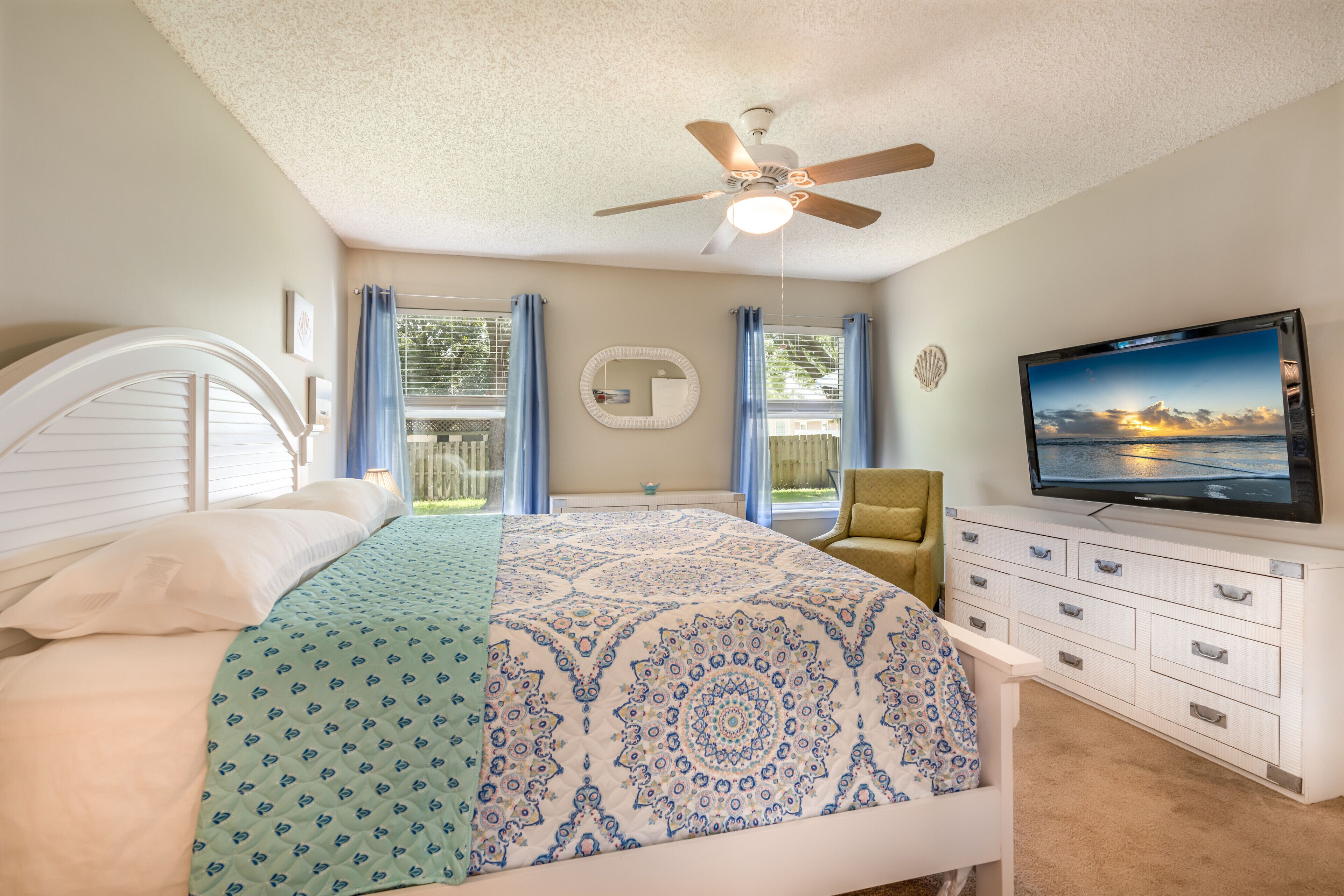 A bedroom with a bed, a ceiling fan, a TV, and a window with curtains.