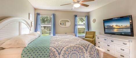 A bedroom with a bed, a ceiling fan, a TV, and a window with curtains.