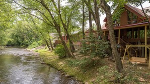 A riverside cabin with a deck and a staircase leading to the upper level. - River Haus - Riverfront Luxury Lodge in Downtown Helen (Helen)