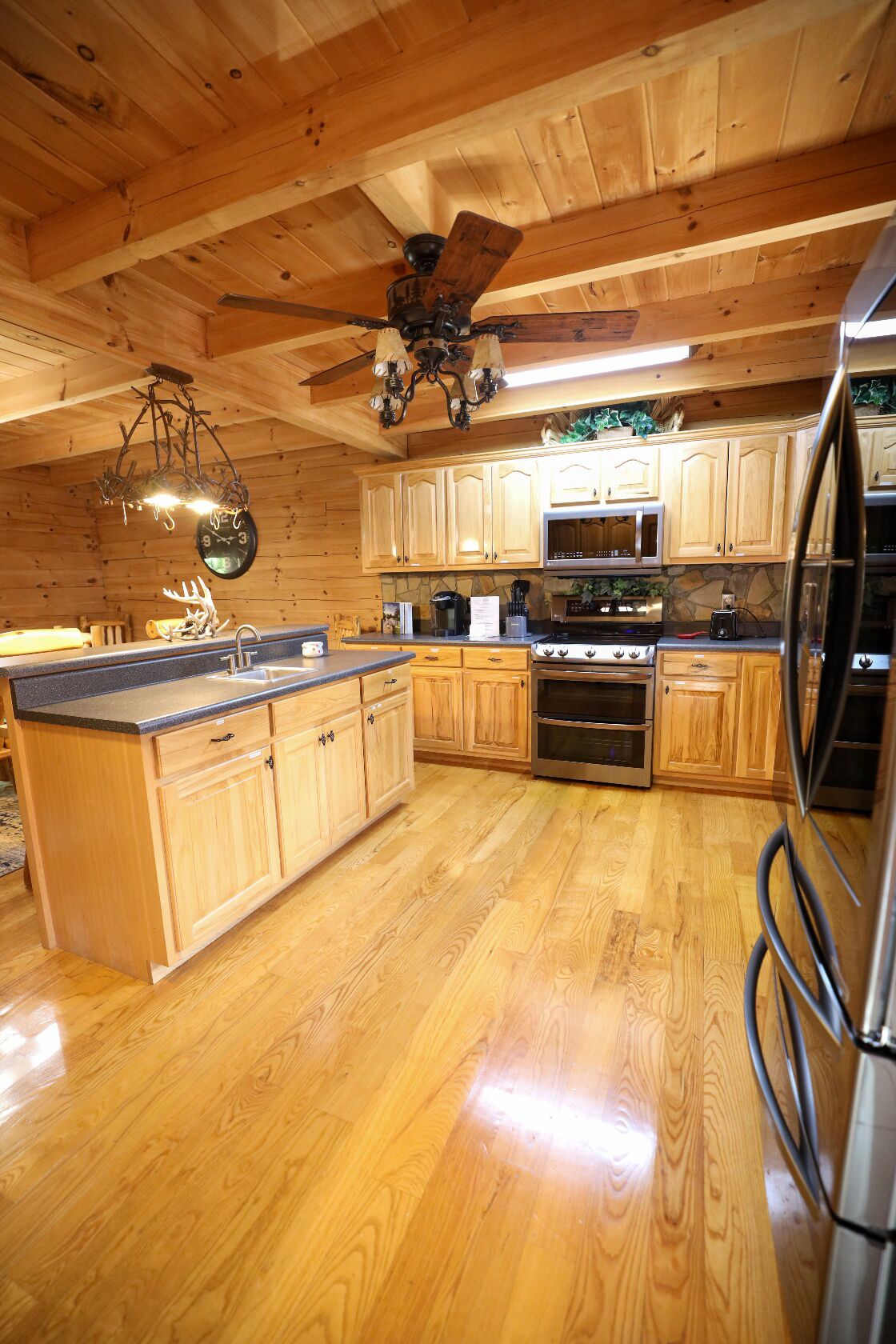 Interno di una baita in legno con cucina, caratterizzata da mobili in legno, un fornello, un forno a microonde e un frigorifero.