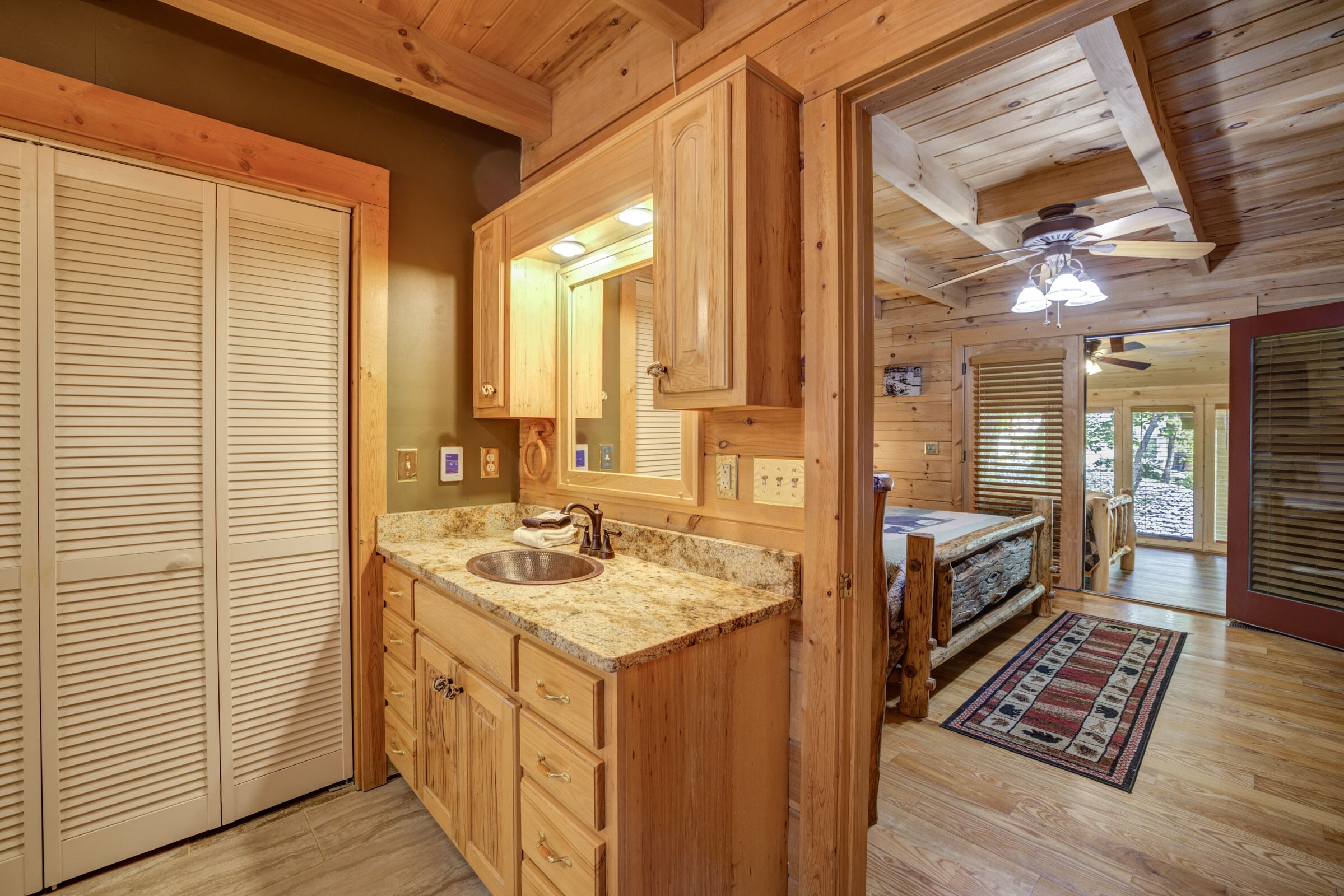 A wooden cabin interior with a kitchen area featuring a granite countertop sink, wooden cabinets, and a ceiling fan.