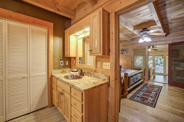 A wooden cabin interior with a kitchen area featuring a granite countertop sink, wooden cabinets, and a ceiling fan.