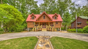 A wooden cabin with a red roof, a porch with yellow railings, and a stone pathway leading to the entrance. - River Haus - Riverfront Luxury Lodge in Downtown Helen (Helen)