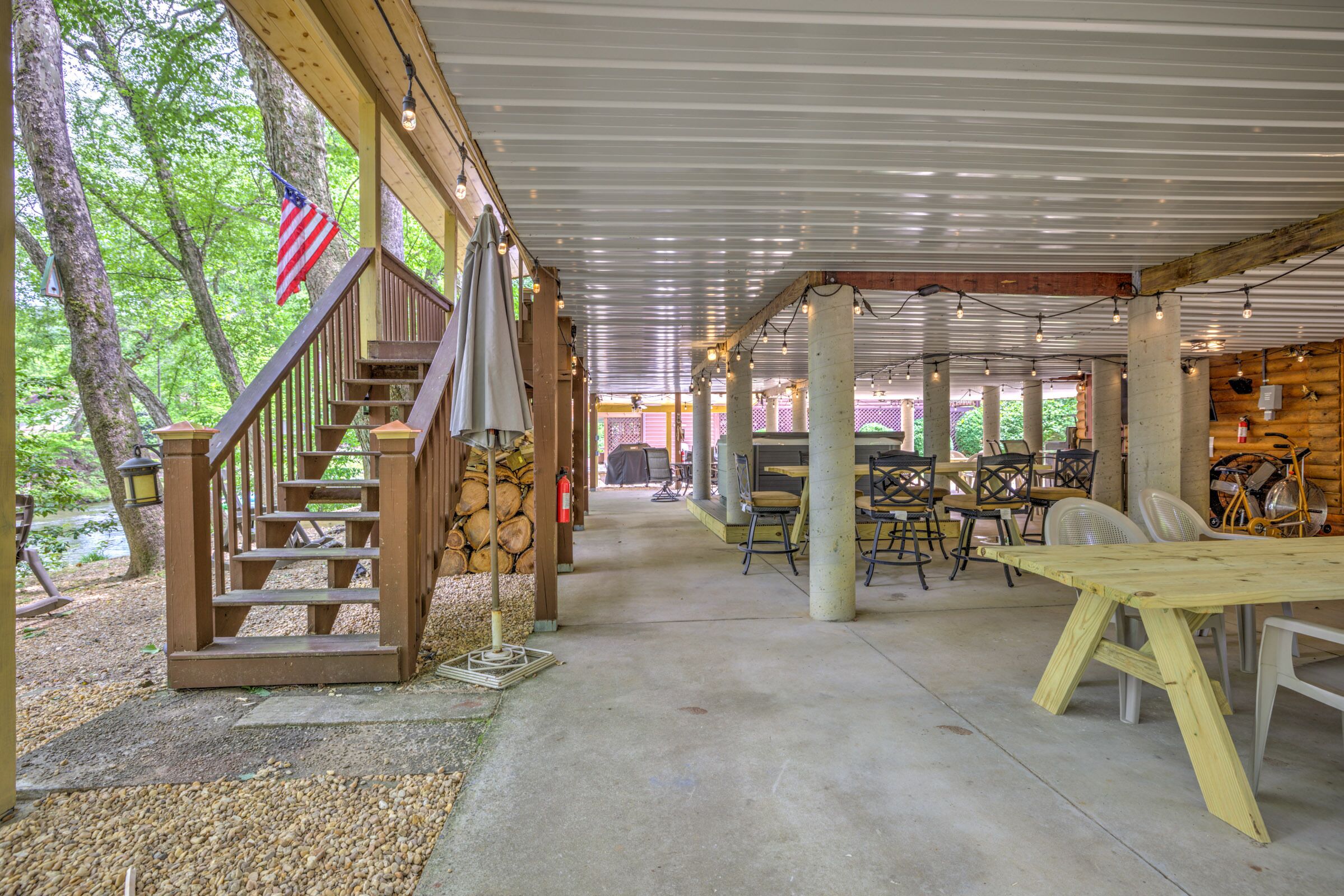 A covered outdoor area with a wooden staircase, tables, chairs, and an American flag.