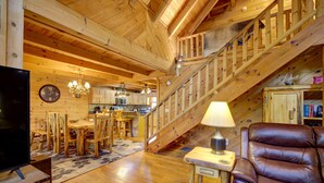A wooden interior with a dining area, a staircase, a leather chair, and a television. - River Haus - Riverfront Luxury Lodge in Downtown Helen (Helen)