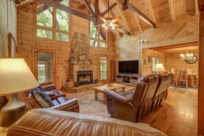 A spacious log cabin interior with a fireplace, leather seating, and a television.